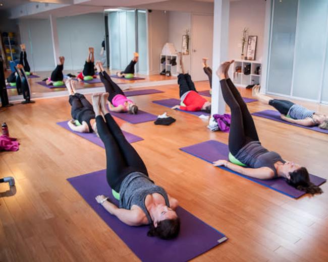Several people are practicing a yoga pose on mats in a spacious studio with natural light.