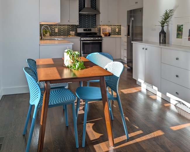 A dining area features a wooden table surrounded by blue chairs, with a modern kitchen in the background.