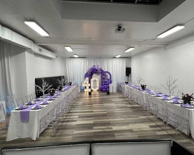 The image shows a decorated banquet hall with two long tables set for a celebration, featuring purple table settings and a large "40" display made of lights.