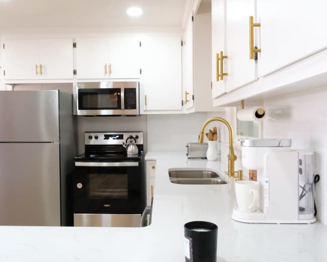 The image features a modern kitchen with white cabinets, stainless steel appliances, and a countertop with a coffee maker and sink.