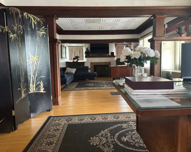 A spacious living area with wooden structural elements, a dark blue sofa, and a decorative screen, leading to a fireplace and television in the background.