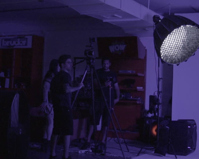 A group of individuals is setting up camera equipment in a dimly lit studio space for a shoot.