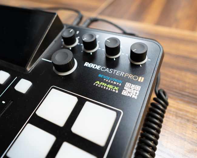 The image shows a Rodecaster Pro II audio production console with several knobs and buttons on a wooden surface.