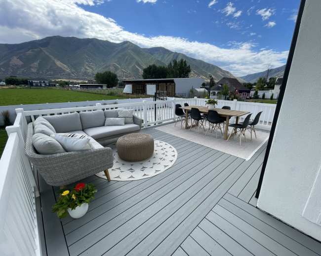 A spacious outdoor deck features a sectional sofa, a round table with chairs, and mountain views in the background.