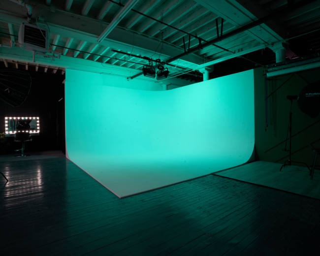 A photography studio with a brightly lit turquoise backdrop and wooden flooring.