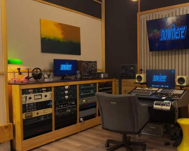 The image shows a modern recording studio with a large desktop workstation, audio equipment, and sound monitors, along with a television displaying the word "nowhere."