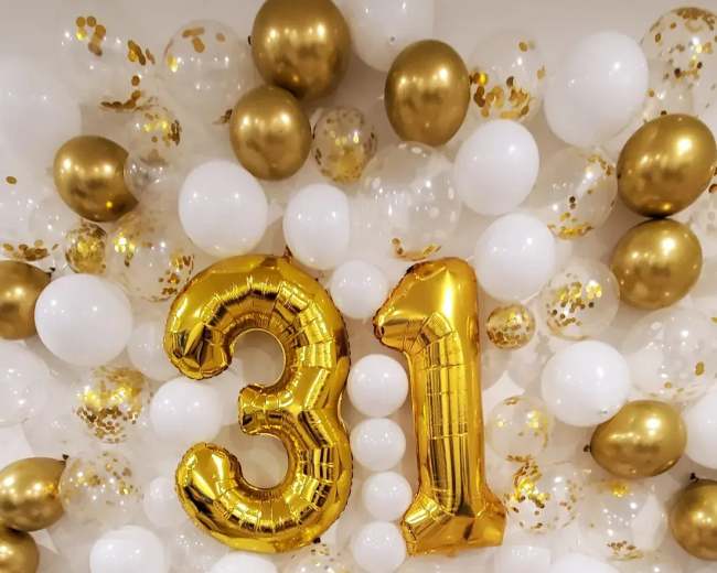 A decorative backdrop of white and gold balloons, with large gold foil numbers "31" centered in the arrangement.