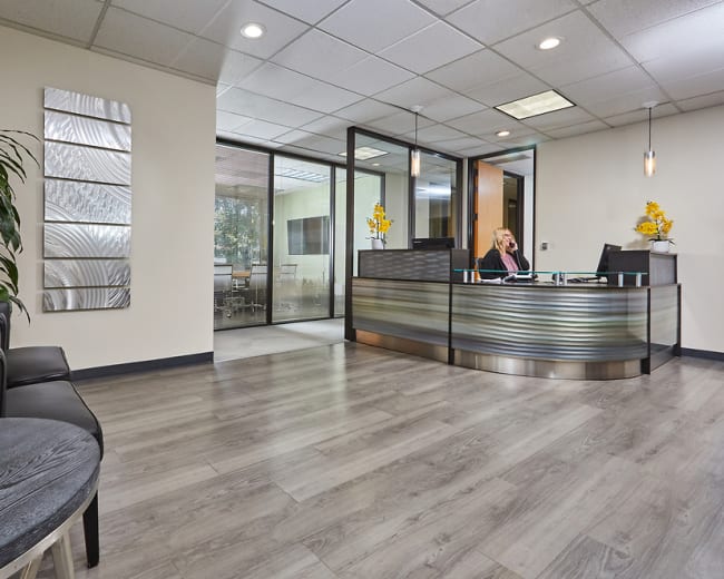 A modern office reception area with a desk, seating, and decorative plants.