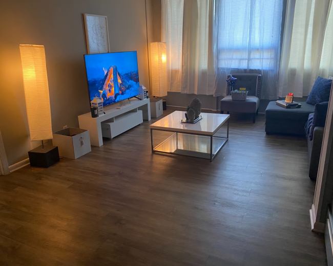 A living room with a large TV displaying a mountain scene, a coffee table, a sofa, and two floor lamps illuminating the space.