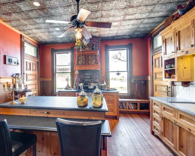The kitchen features wooden cabinetry, a central island with a black countertop, and a ceiling adorned with decorative tin tiles.