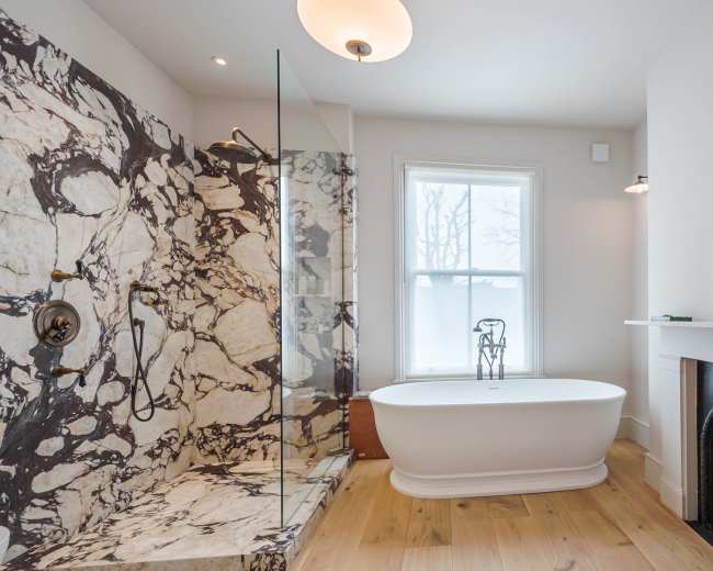 The image shows a modern bathroom featuring a freestanding tub, a marble shower enclosure, and a decorative fireplace.