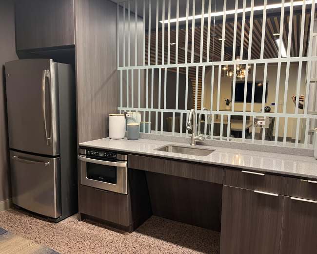 A modern kitchen area featuring stainless steel appliances, a sink, and a countertop, with a partition of vertical bars in the background.