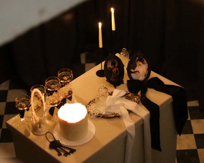 A table is adorned with glasses, candles, and decorative items, including photos in ornate frames and a lit cake.
