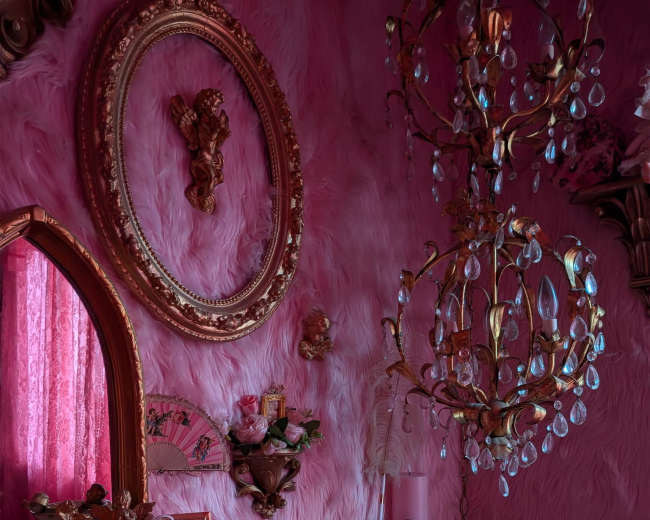 The scene features a pink-themed room with plush walls, ornate decor, and a chandelier, alongside various framed mirrors and floral arrangements.