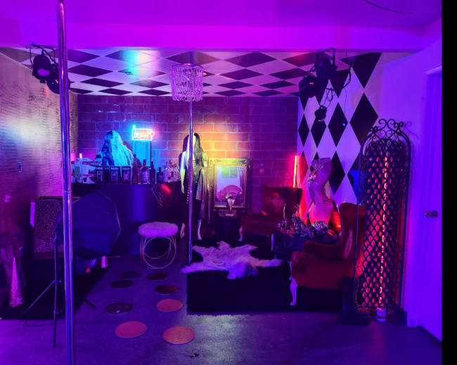 The scene features a colorful room with neon lights, a mirrored pole, a checkered ceiling, and various decorative elements, including furniture and wall art.