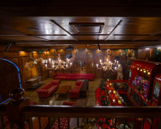 The image shows a dimly lit bar area with red tufted seating, a wooden ceiling, and a decorative bar featuring various bottles.