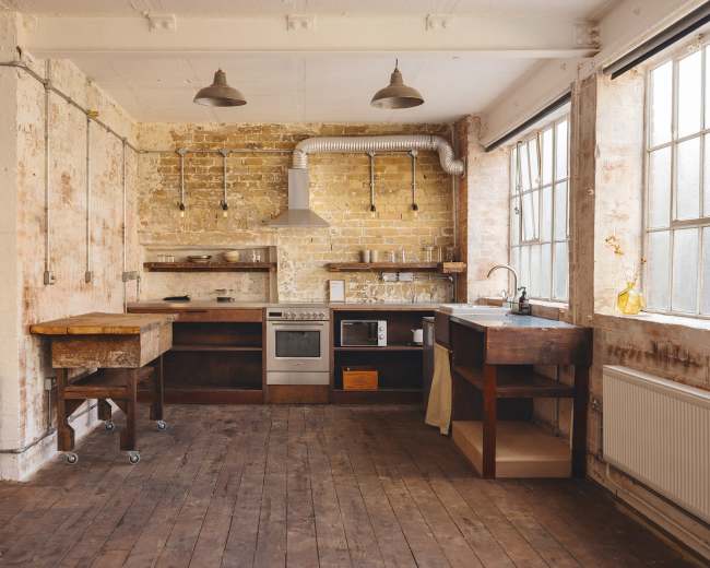 The kitchen features exposed brick walls, a wooden floor, and industrial-style lighting, with modern appliances and wooden countertops.