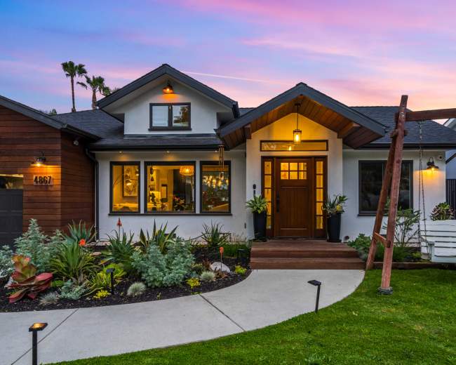 A contemporary home with a wooden front door and a swing hangs in the front yard, surrounded by landscaped greenery and a pathway leading to the entrance.