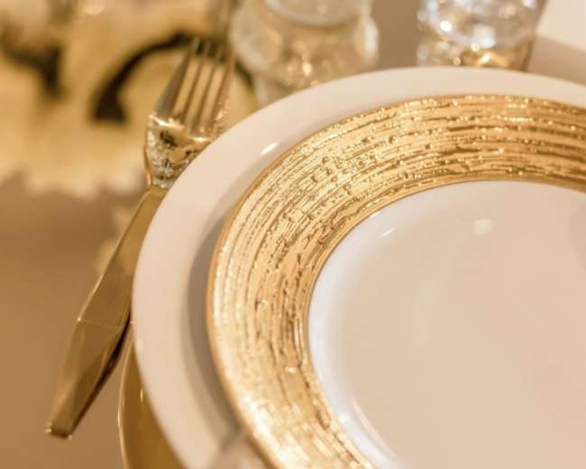 A white plate with a textured gold rim is set on a table beside a fork and a glass.