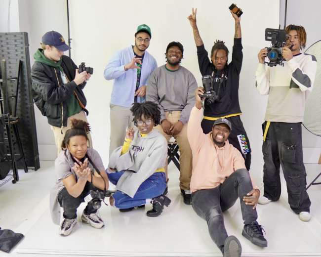 A group of eight people poses in a studio with cameras and lighting equipment.