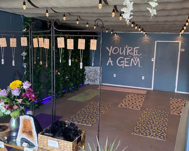 A cozy room with a decorative ceiling, string lights, a flower arrangement, gemstones for sale, and yoga mats arranged on the floor.