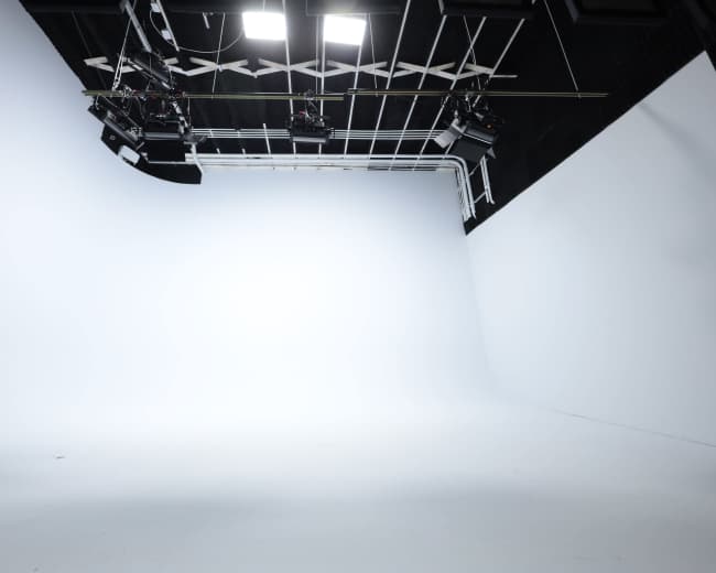 A large, empty photography studio with seamless white backdrops and overhead lighting equipment.