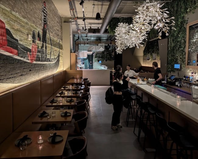 The image shows a modern restaurant interior with a bar, seating area, and decorative wall art.