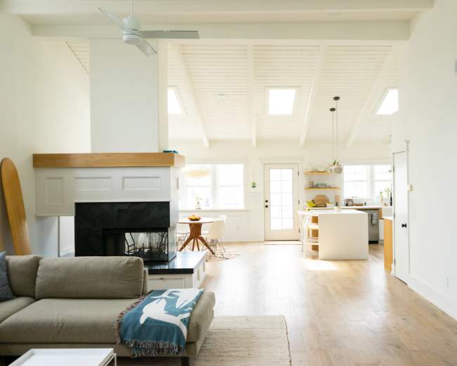 A bright, open living area features a sofa, a fireplace, and a view into a modern kitchen with a dining table.