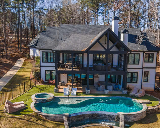 A spacious modern house with a black and white exterior features a pool and hot tub, set in a wooded area.