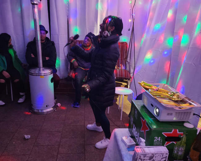 A person in a black coat dances under colorful lights in a decorated space with tables of snacks and drinks.