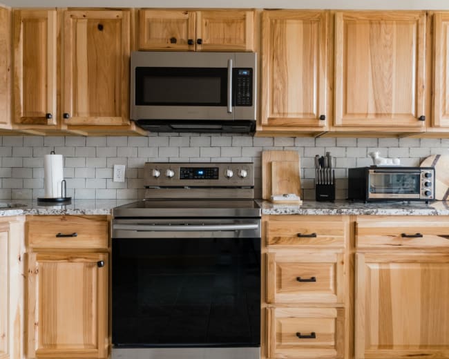 A modern kitchen with wooden cabinets, a stainless steel microwave, and an oven set against a tiled backsplash.