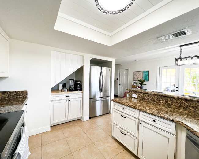 A modern kitchen features white cabinets, a granite countertop, and stainless steel appliances, with a skylight illuminating the space.
