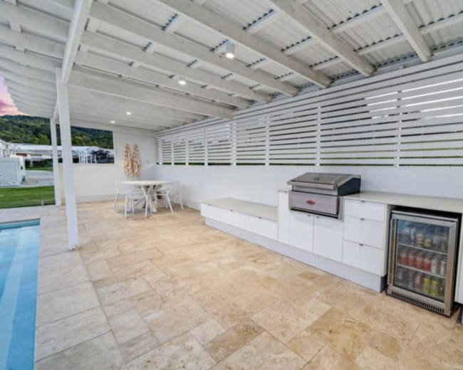 The image shows a patio area with a grill, countertop, and beverage refrigerator alongside a swimming pool.