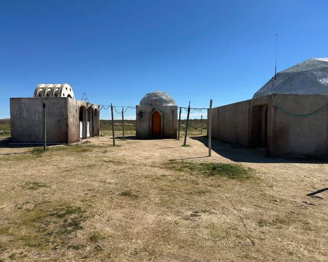 The image shows a barren landscape with three unique structures, two of which have domed roofs, and a series of clotheslines in between.