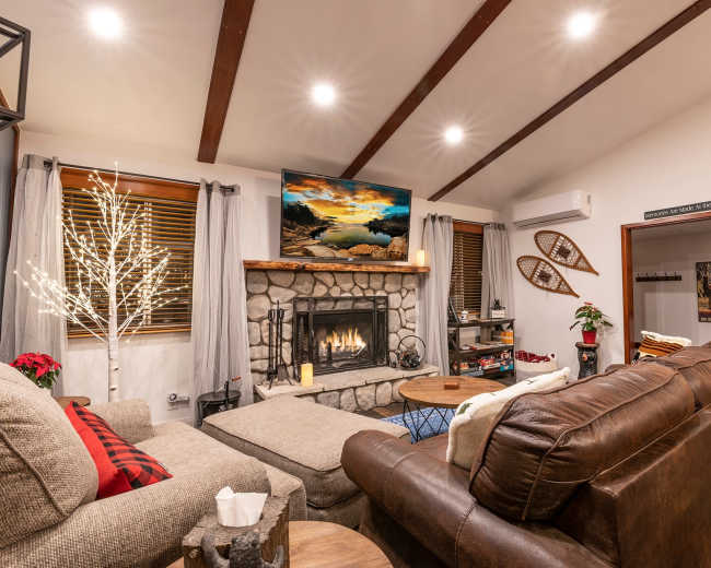 A cozy living room with a stone fireplace, a television mounted above it, and comfortable seating arranged around a coffee table.
