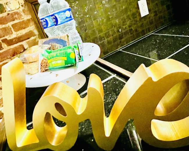 A gold "love" sign is positioned in front of a small table with snacks and bottled water.