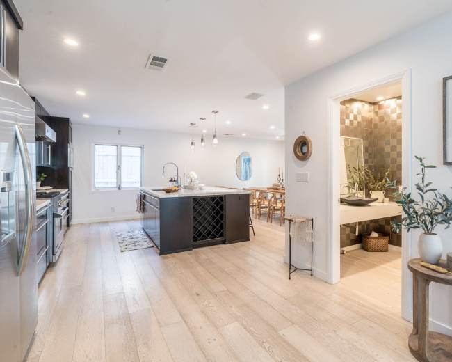 The image shows a modern kitchen and dining area with a large island, a dining table, and a doorway leading to a bathroom.