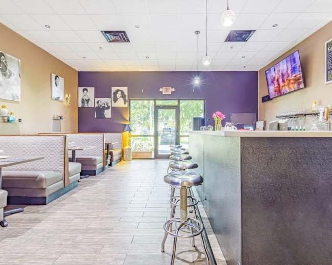 The image shows the interior of a modern café featuring seating booths along one wall and a bar counter facing a glass entrance.