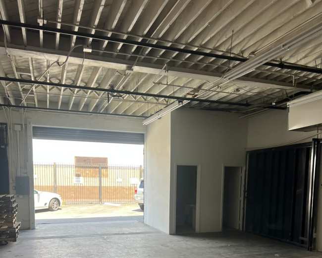 The image shows an empty industrial space with concrete flooring, a partially enclosed area, and a large open entrance leading outside.