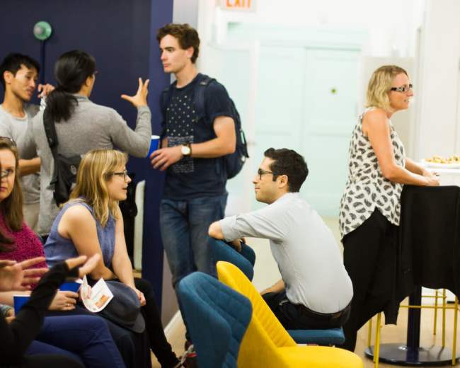 A group of people socialize in a modern interior space with colorful seating and casual furniture.