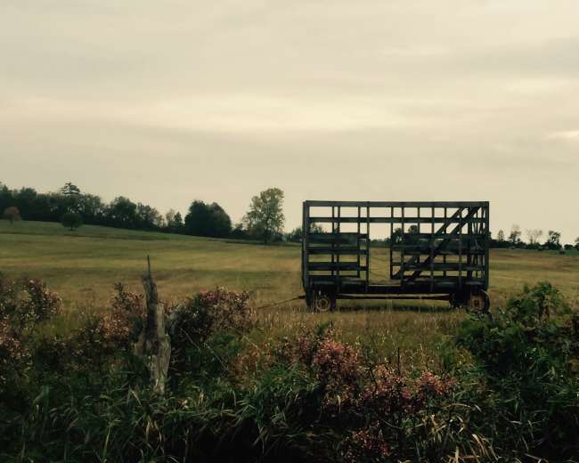 A metal trailer sits on a grassy field under a cloudy sky.