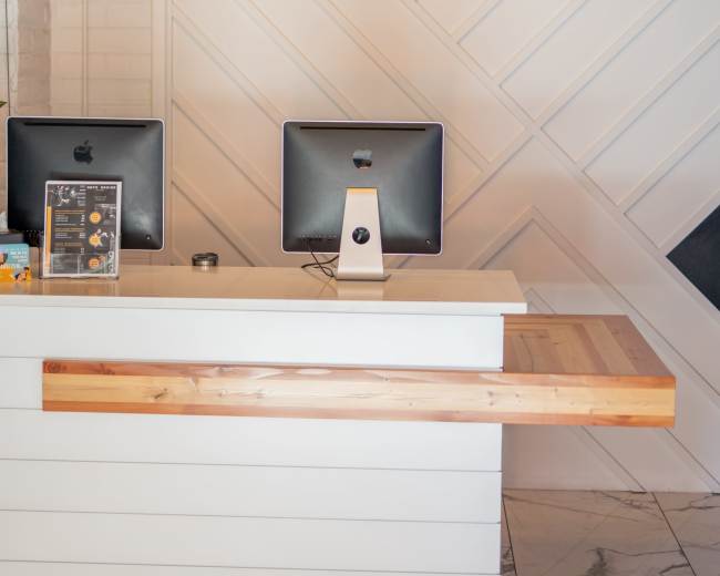 A modern reception desk with two computer monitors facing a white and wood-paneled wall.