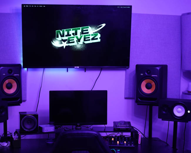 The image depicts a music production setup featuring a large screen displaying "NITE EYEZ," flanked by studio monitors and a computer workstation.