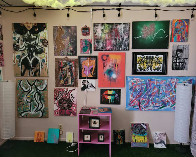 A room with a collection of various artworks displayed on the walls, accompanied by a pink table and decorative lamps.