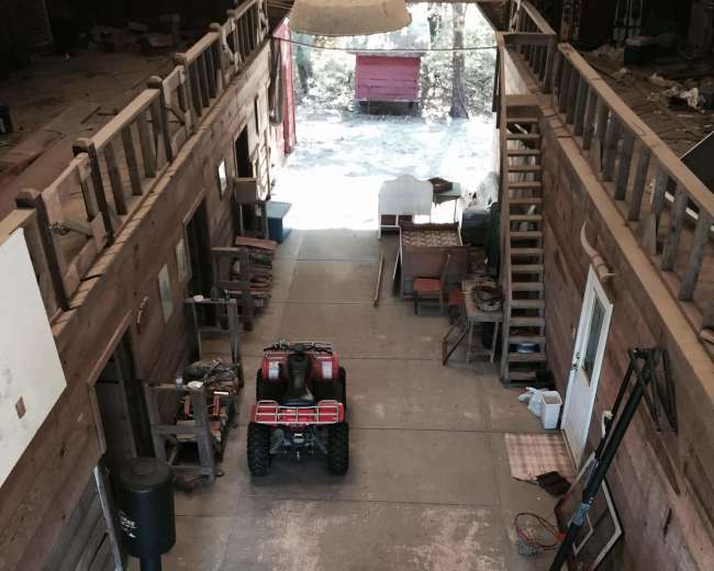 A spacious, unfinished interior of a barn-like structure with an ATV parked in the center, surrounded by various items and wooden beams overhead.