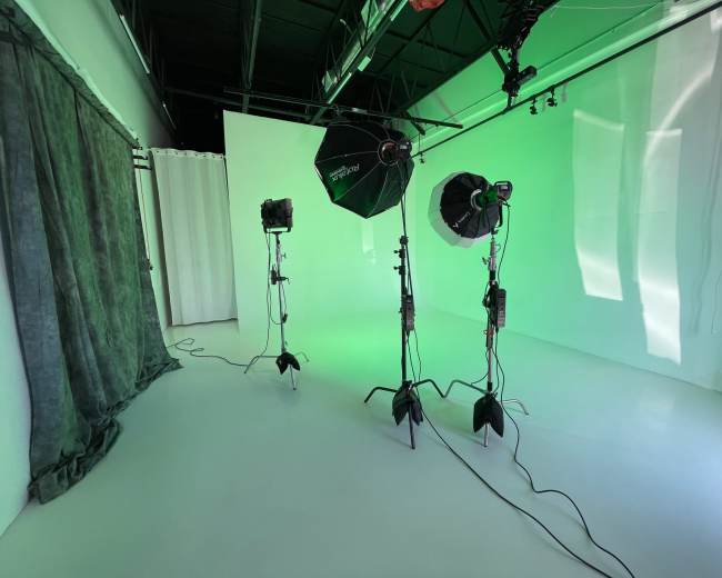 The image shows a photography studio with three light stands positioned in front of a green backdrop and a white wall.