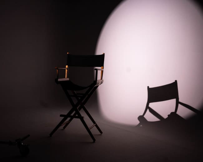 A director's chair is positioned in a dimly lit studio, casting a shadow on the floor.