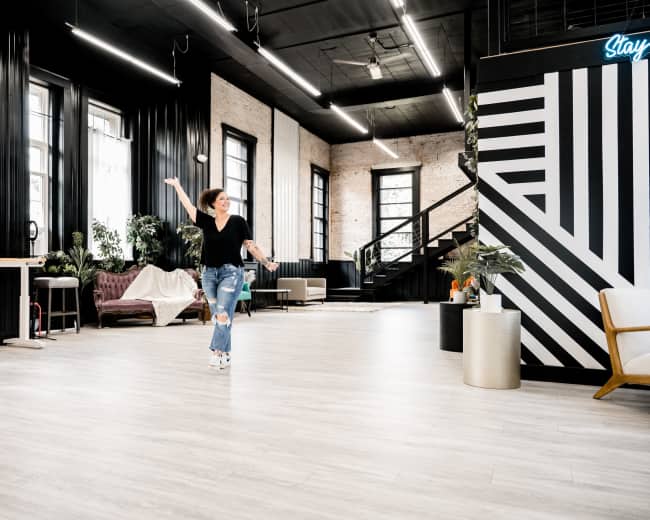 A woman is dancing in a spacious, modern interior with black and white walls, large windows, and various plants.
