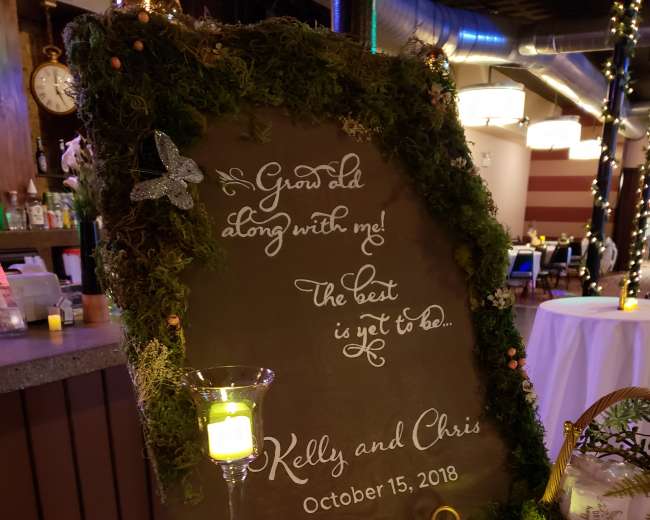 A decorated welcome sign surrounded by greenery and candles announces the wedding of Kelly and Chris on October 15, 2018.