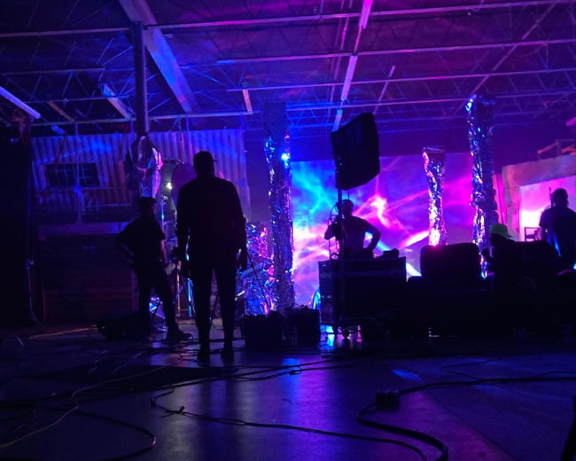 A group of silhouetted figures work in a dimly lit space filled with colorful, dynamic lighting effects and equipment.